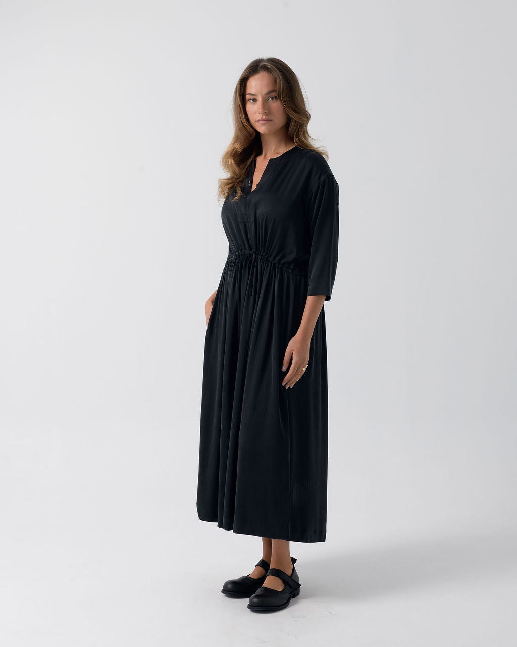 Side view of the Washed Black Drawstring Dress with a drawstring waist, three-quarter sleeves and fluid drape.