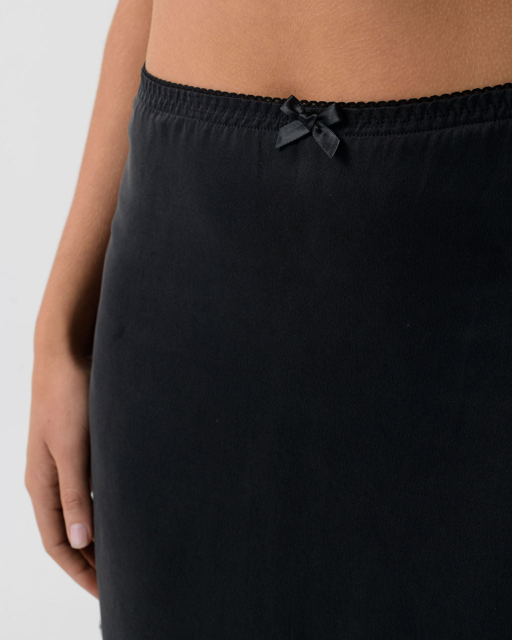 Close-up of the Washed Black Mini Skirt showing the elastic waistband with satin bow detail and stonewashed stretch silk fabric.