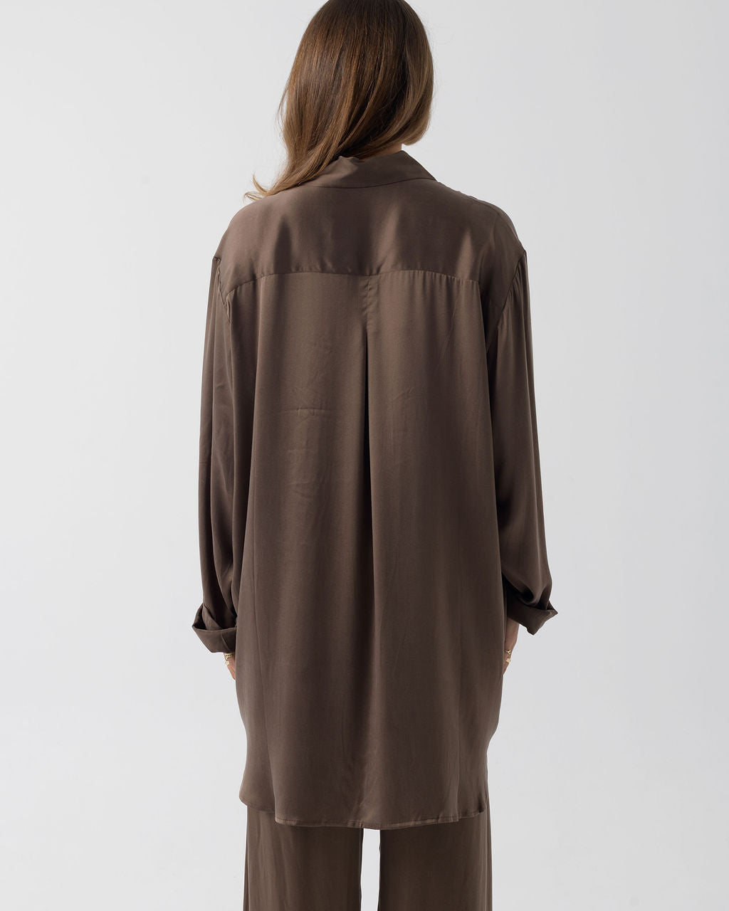 Model wearing the Hazelnut Oversized Silk Shirt in stretch silk, shown from the back with a relaxed oversized silhouette.