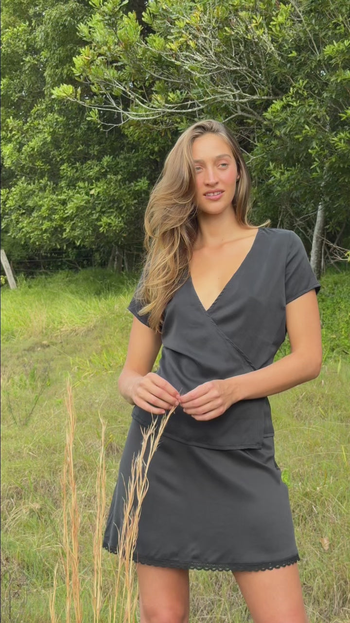 Model wearing the Washed Black Mini Skirt in stonewashed stretch silk with a fluid slip silhouette, delicate cotton lace trim and elastic waistband with satin bow detail.
