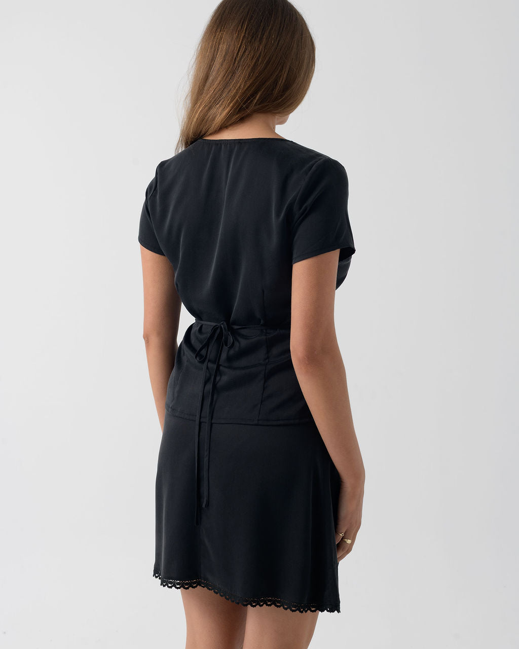 Back view of the Black Short Sleeve Wrap Blouse in stonewashed stretch silk with an adjustable waist tie and relaxed fit.