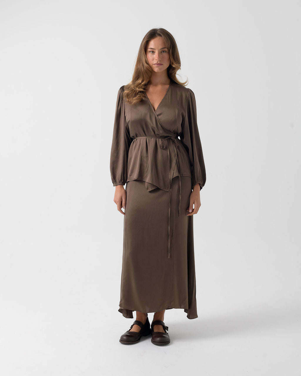 Model wearing the Moka Wrap Blouse in stonewashed stretch silk with billowed sleeves, a wrap silhouette and waist tie.